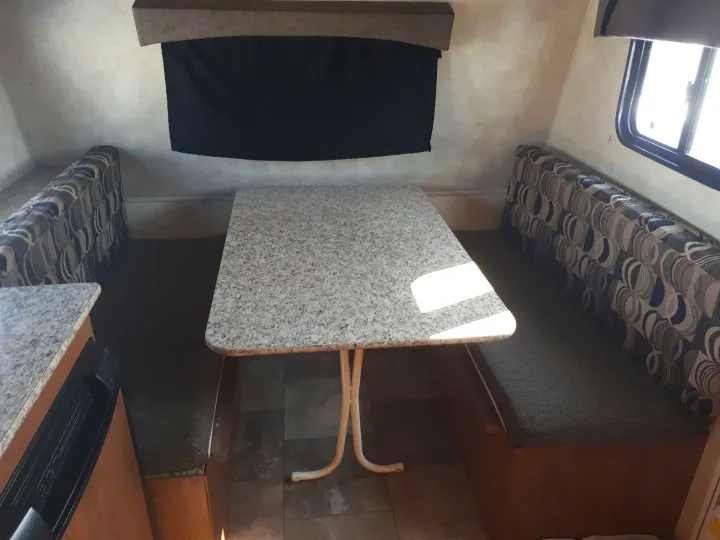 Spacious RV rental dinette with speckled table and patterned benches, illuminated by a bright window.. Coachmen Clipper 2013