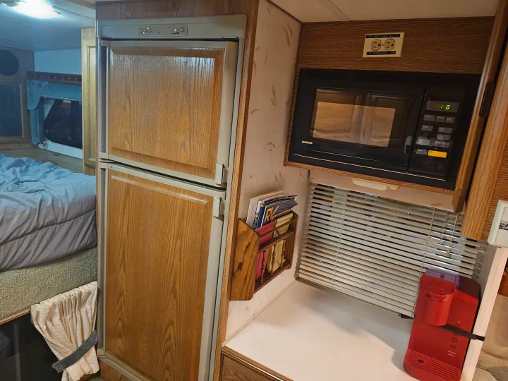RV rental interior: A compact space with a wood-paneled refrigerator, microwave, Keurig, and bed.. Lance legend 880 2018