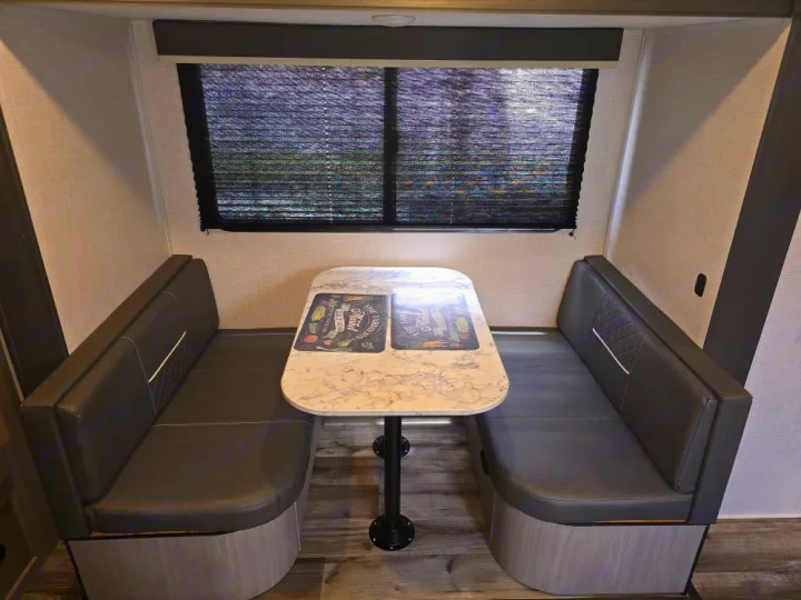 RV rental dinette: cozy seating with two dark benches, a white marble table, and a window. Ideal for meals.. Coleman 1855RB 2022