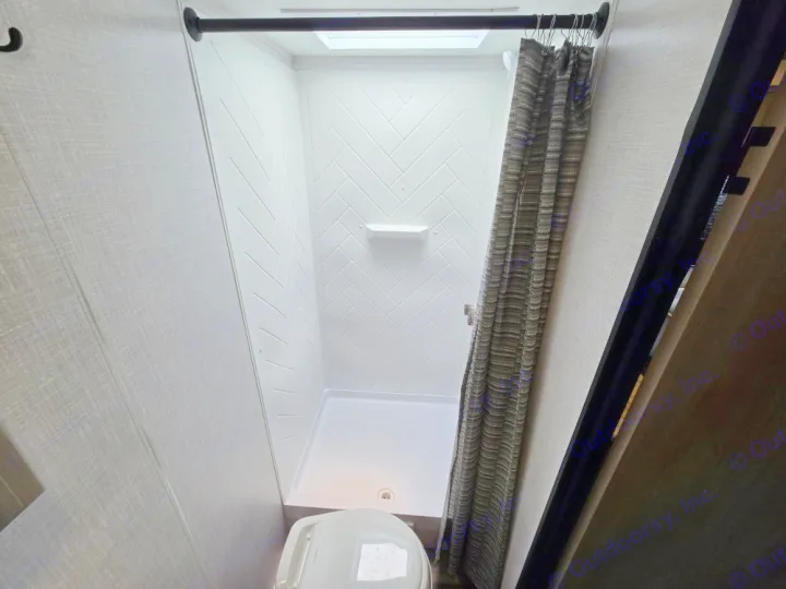 Clean RV rental bathroom featuring a white shower with herringbone walls, skylight, and toilet for your comfort.. Coleman 1855RB 2022