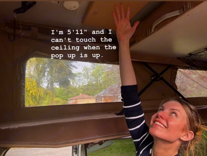 Woman at 5'11" reaches for the high ceiling in a pop-up RV rental, demonstrating ample headroom when extended.. Sportsmobile Regular Body 2013