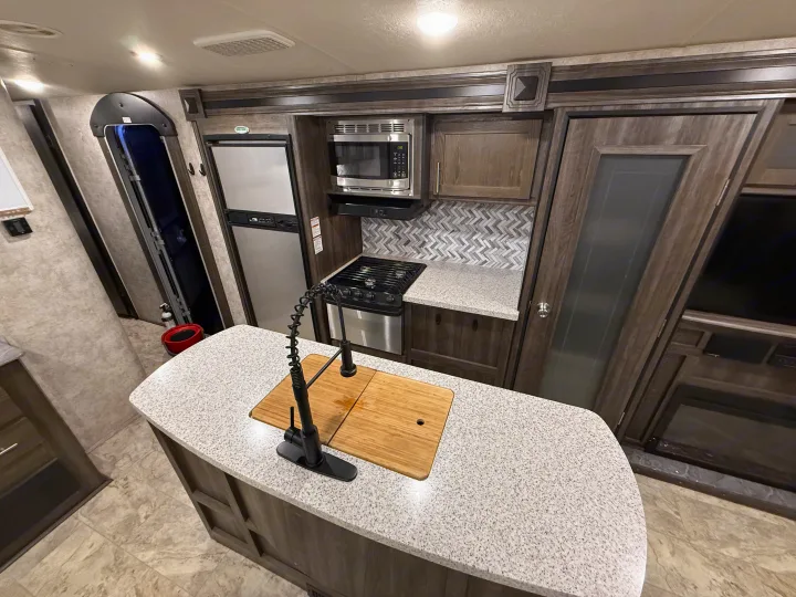 Modern RV rental kitchen interior with island sink, stove, microwave, and refrigerator for convenient living on the go.. Highland Ridge RV Light 2018