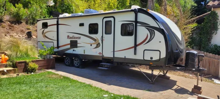 This RV rental travel trailer is parked on a paved area in a lush backyard, ready for your next adventure.. Cruiser RV Radiance 2015