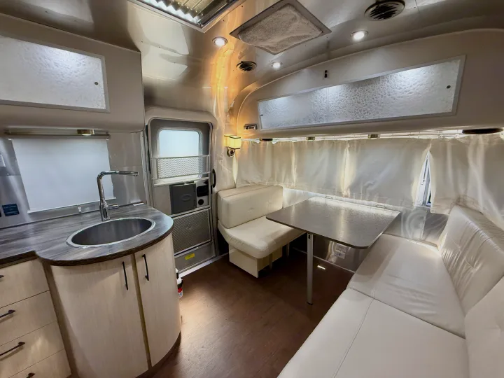 Modern RV rental interior featuring a kitchen with a sink, dining area with a table, and cozy white bench seating.. Airstream 27FBINT 2017
