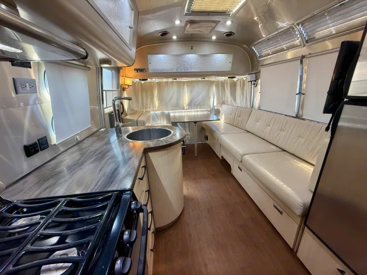 Spacious RV rental interior showcasing a modern kitchen with sink and stove, plus a comfortable dinette area.. Airstream 27FBINT 2017
