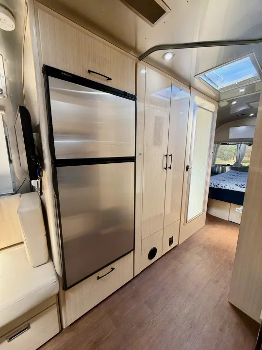 Bright and modern RV rental interior featuring a stainless fridge, ample cabinetry, shower, and a cozy bedroom.. Airstream 27FBINT 2017