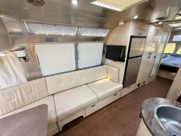 Modern Airstream RV rental interior featuring L-shaped seating, kitchen, and a glimpse of the cozy bedroom. Spacious living.. Airstream 27FBINT 2017