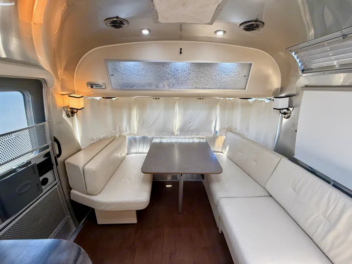 A bright, clean RV rental interior featuring a U-shaped dinette with white leatherette benches and table.. Airstream 27FBINT 2017