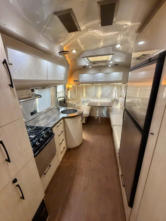 Modern RV rental interior with a fully equipped kitchen, dining booth, and large refrigerator.. Airstream 27FBINT 2017