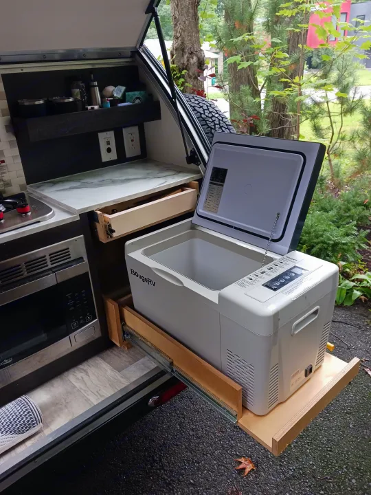 Compact outdoor kitchen in an RV rental, featuring a fridge slide-out, microwave & stove for easy camping.. nuCamp T@G 2023