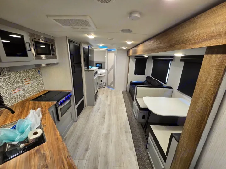 Inside a stylish RV rental: view of the kitchen, dining booth, and living space. Light wood floors, dark accents. Ready for your trip.. Heartland North Trail 29BHP 2022