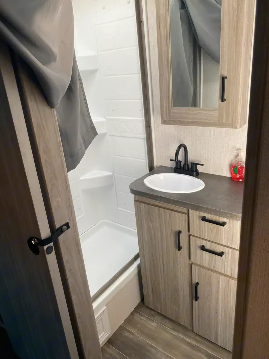 Modern rv rental bathroom featuring a shower, vanity, and cabinet storage.. Keystone RV Passport GT 2022
