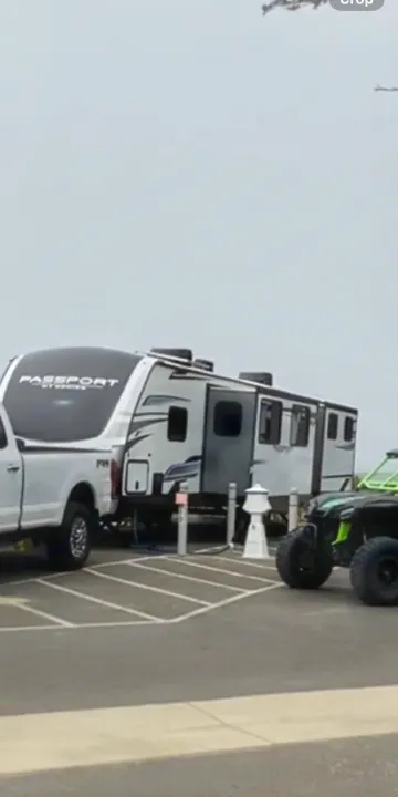 White pickup truck and a Passport travel trailer RV rental set up at a camp spot. A green off-road vehicle is beside it.. Keystone RV Passport GT 2022