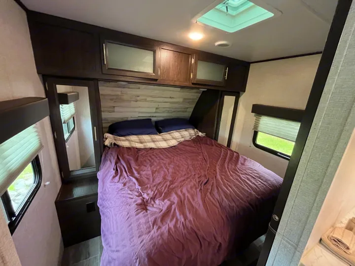 Spacious RV rental bedroom featuring a cozy bed with purple bedding, overhead cabinets, and windows.. Dutchmen Kodiak Ultra Lite 2020