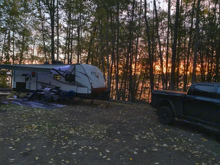 Kodiak RV rental and black truck at a serene campsite with autumn leaves and sunset through trees.. Dutchmen Kodiak Ultra Lite 2020
