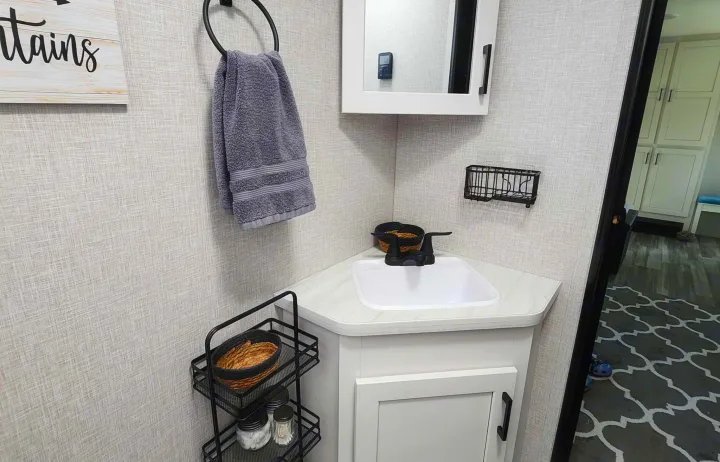 Compact RV rental bathroom features a corner sink vanity, mirrored cabinet, towel ring, and tiered storage shelves for essentials.. Jayco Jay Flight 2024