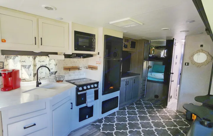 Modern RV rental kitchen with white cabinets, black appliances, sink, and comfortable bunk beds for family trips.. Jayco Jay Flight 2024