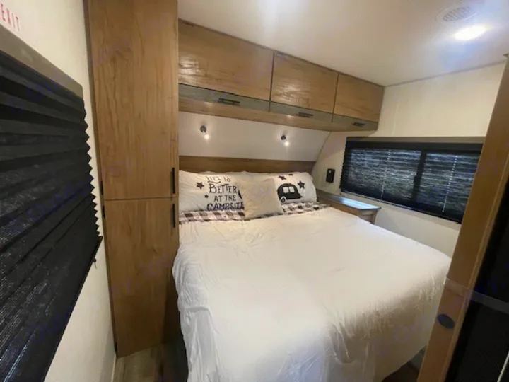 Cozy RV rental bedroom featuring a white bed, overhead cabinets, and a compact wardrobe. Ideal for road trips.. Forest River Campsite Reserve 26CJ 2025
