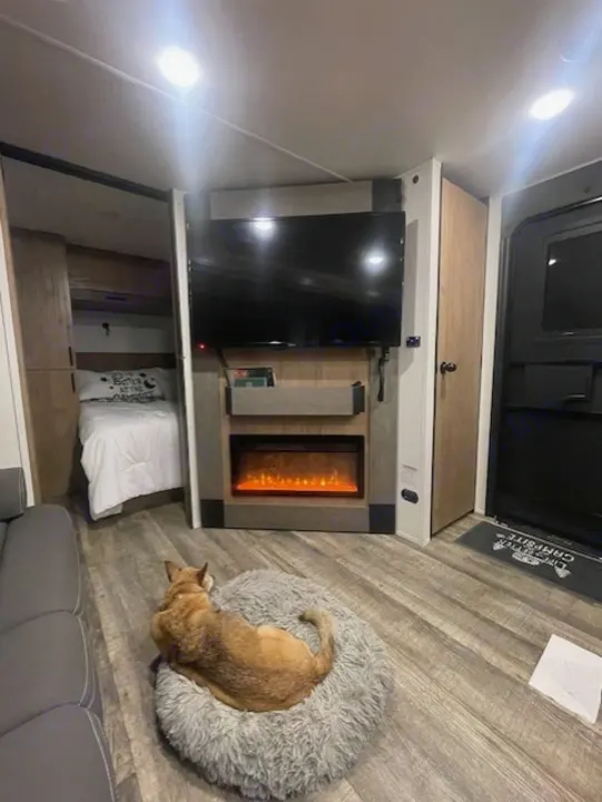 Inside an RV rental: a comfortable living area with a dog on its bed, TV, and glowing electric fireplace.. Forest River Campsite Reserve 26CJ 2025