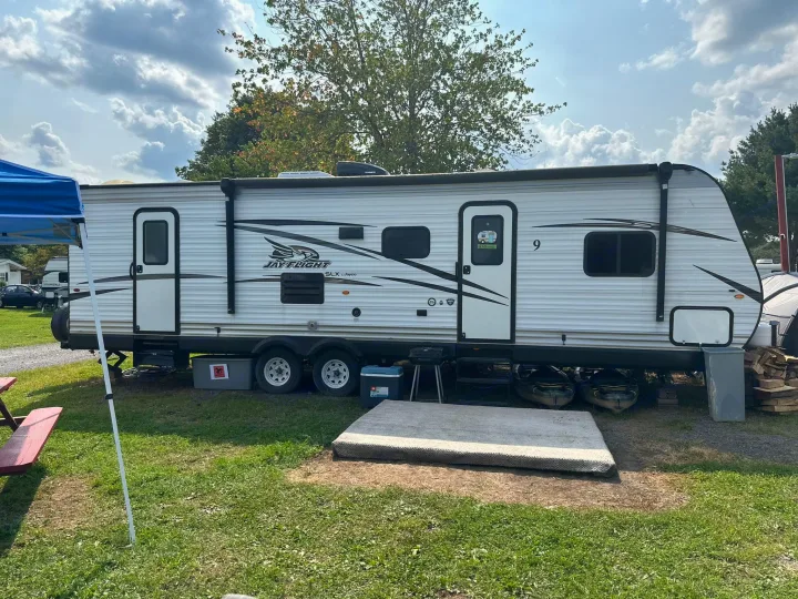 Serene campsite featuring a Jayco travel trailer rv rental setup. Perfect for outdoor adventures with picnic table & kayaks.. Jayco Jay Flight 2018