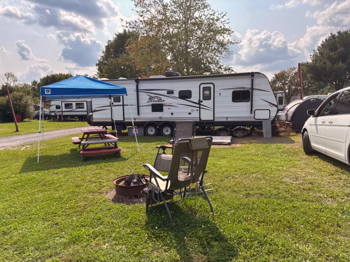 Enjoying a spacious RV rental campsite with a white RV, blue canopy, picnic table, and fire pit on a sunny day.. Jayco Jay Flight 2018
