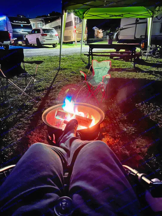 Relaxing at an RV rental campsite. Feet propped by a vibrant campfire, with travel trailers and RVs under the night sky.. Jayco Jay Flight 2018