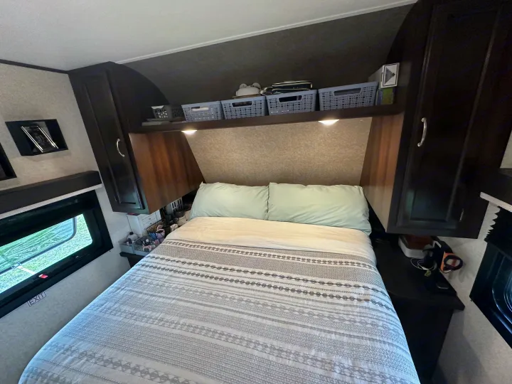 Cozy RV rental bedroom featuring a patterned bed, overhead storage, and windows with an "EXIT" sign.. Jayco Jay Flight 2018