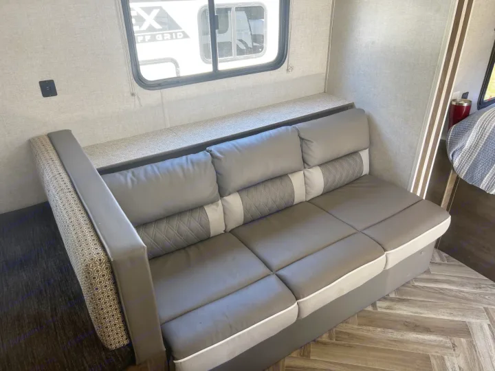 RV rental features: cozy gray sofa with accent pillows, built-in shelf, USB charging port, and window view.. Forest River Wildwood 2021
