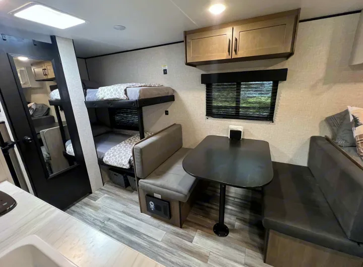 An RV rental's interior with stacked gray bunk beds, a dark dinette seating area, and a functional kitchen counter.. Jayco Jay Flight SLX 170BHW 2025