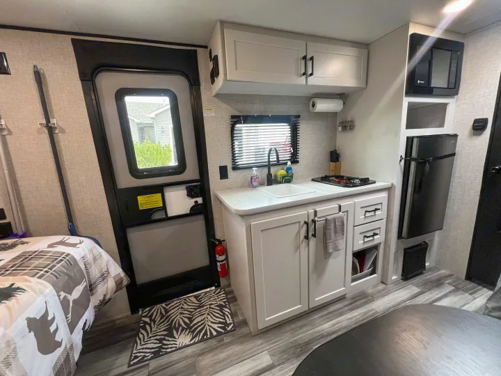 RV rental interior showing a compact kitchen with sink, stove, microwave, fridge, an entrance door, and a bed area.. Jayco Jay Flight SLX 170BHW 2025