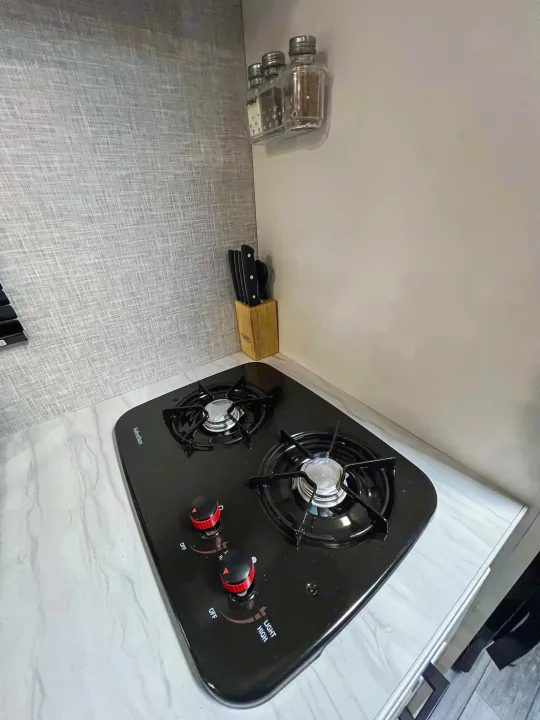 Compact RV rental kitchen with 2-burner Suburban gas stovetop, knives, & wall-mounted spices.. Jayco Jay Flight SLX 170BHW 2025