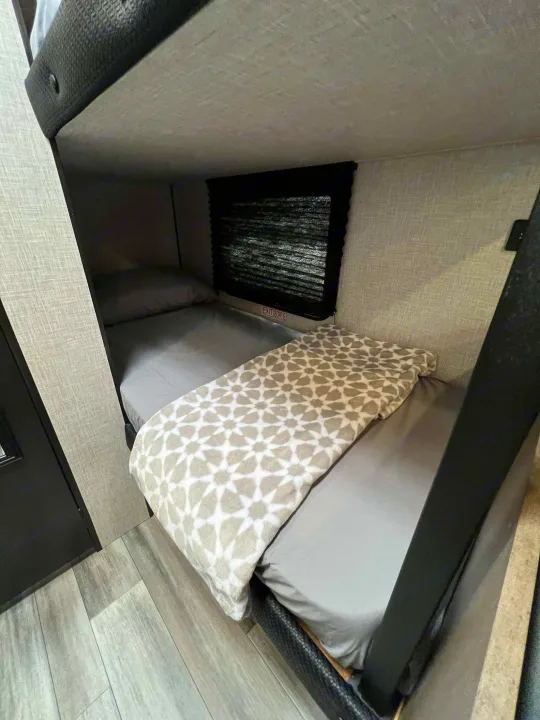 Cozy RV rental interior with bunk beds. Lower bunk has grey sheets & a patterned blanket. An exit window is visible.. Jayco Jay Flight SLX 170BHW 2025