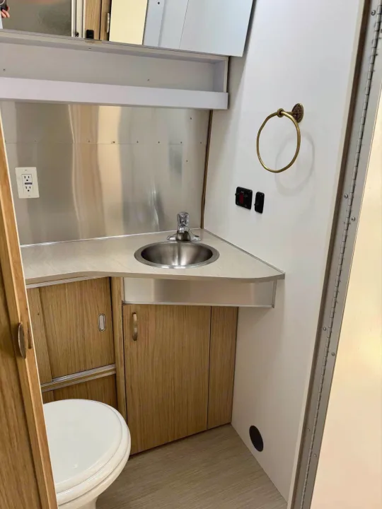 This RV rental's compact bathroom features a stainless steel sink, wooden vanity, and toilet, showing efficient use of space.. Airstream Flying Cloud