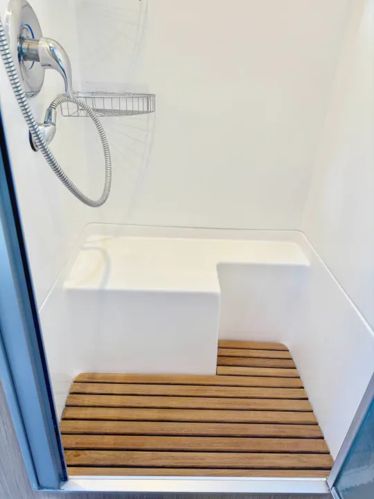 Compact RV rental shower featuring a white built-in seat and a warm wooden slatted mat for comfort.. Airstream Flying Cloud