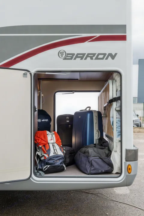 The opened storage of a "BARON" RV rental, showing various suitcases, backpacks, and duffel bags inside.. Elnagh baron 20 2025