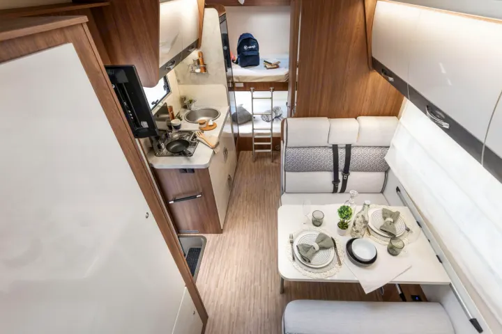 Bright, modern RV rental interior featuring a compact kitchen, dining area, and bunk beds at the rear. Ideal for trips.. Elnagh baron 20 2025
