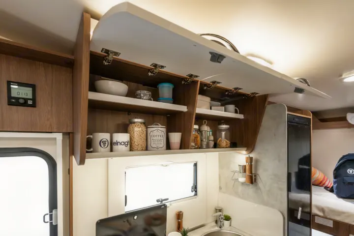 Well-equipped RV rental kitchen featuring open overhead storage, sink, compact fridge, and a control panel for comfortable travel.. Elnagh baron 20 2025