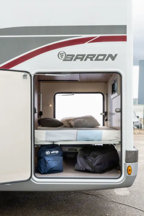 Inside an RV rental, a large open storage compartment reveals a comfortable bed above and luggage bags below. Ideal for travel.. Elnagh baron 20 2025