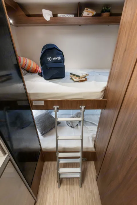 RV rental interior features cozy bunk beds with a ladder. A backpack & books are on the top bunk, a pillow on the bottom.. Elnagh baron 20 2025