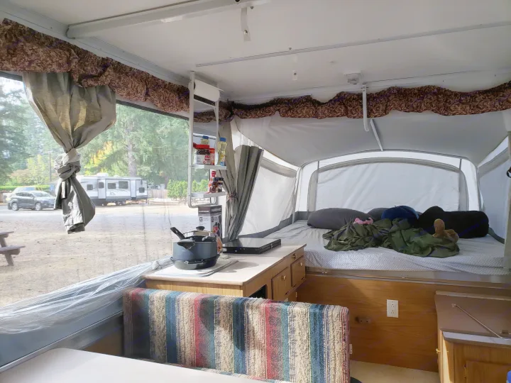 Cozy pop-up camper rv rental interior, featuring a bed, kitchen, and dining area with a view of a serene campsite.. Coleman Sedona 1999