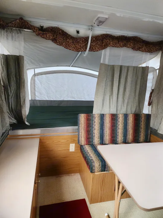 Cozy RV rental pop-up camper interior, showing striped dinette cushions, wooden cabinets, and bed area.. Coleman Sedona 1999