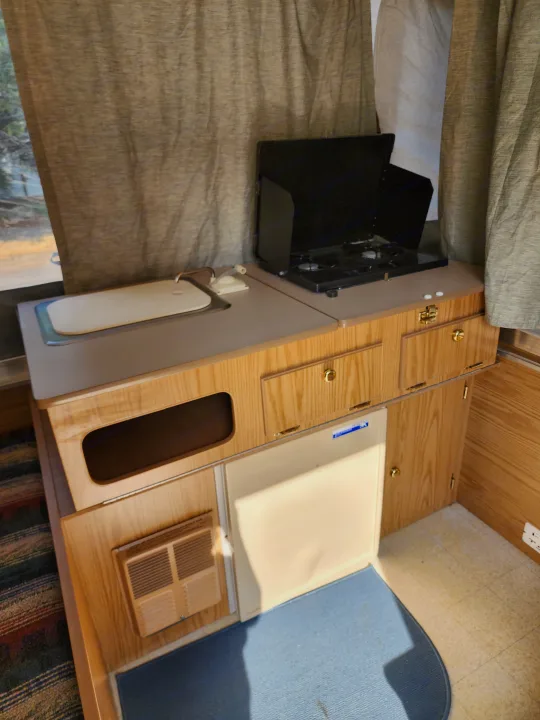 RV rental's compact kitchen setup: sink, two-burner stove, refrigerator, and wood cabinets. Ready for your next camping trip.. Coleman Sedona 1999