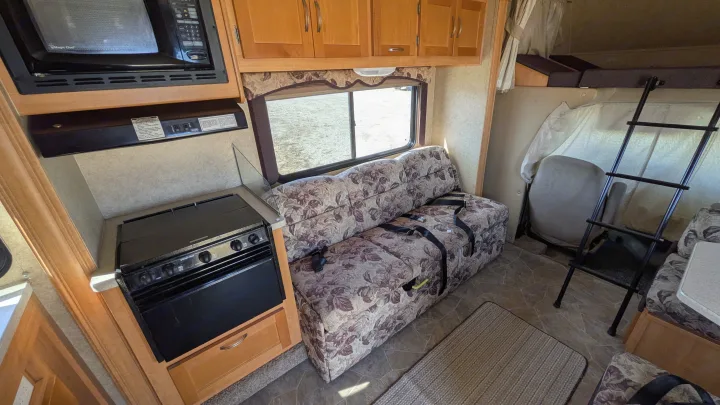 RV rental interior featuring a full kitchen with microwave and oven, comfortable couch/sleeper, and ladder to the overhead bunk.. Forest River Sunseeker 2010