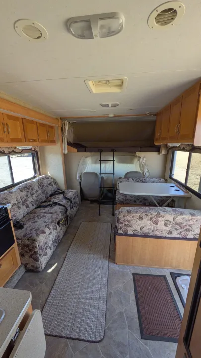 Spacious RV rental interior featuring a cozy dinette, patterned sofa, and overhead bunk.. Forest River Sunseeker 2010