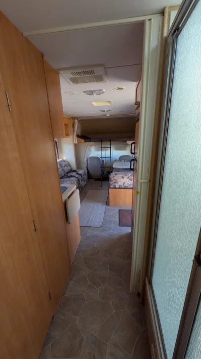 Inside an RV rental: compact living space with wood cabinetry, patterned seating, and a bathroom door visible.. Forest River Sunseeker 2010