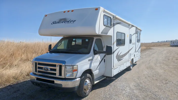 White Sunseeker RV rental parked on a gravel lot with dry grass and blue sky. Ideal motorhome for adventures.. Forest River Sunseeker 2010