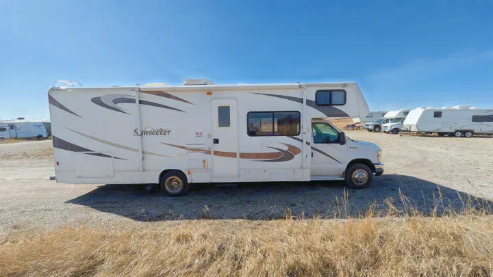 White Sunseeker RV rental (Class C motorhome) parked on a gravel lot under blue sky. Perfect for road trips.. Forest River Sunseeker 2010