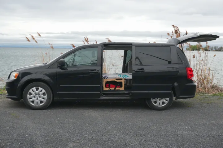 Black camper van conversion by the water with open side door showing custom bed. Ready for your RV rental adventure.. Dodge Grand Caravan 2014
