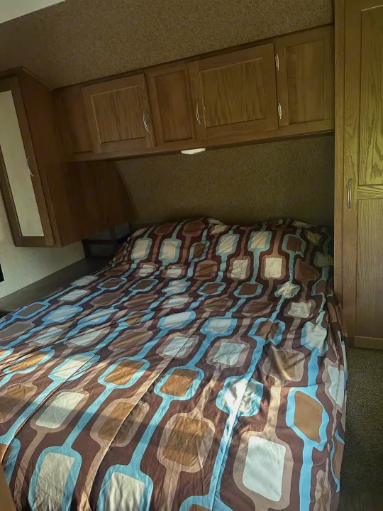 Cozy RV rental bedroom with geometric patterned bed, wood cabinets, and wardrobe for a relaxing getaway.. Gulf Stream Conquest 2017