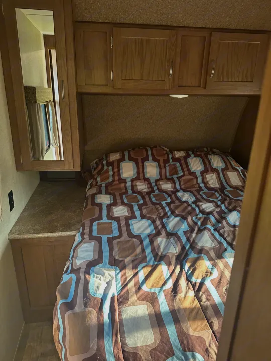 Cozy RV rental bedroom: bed with brown/blue patterned comforter, wood cabinets, and bedside counter.. Gulf Stream Conquest 2017